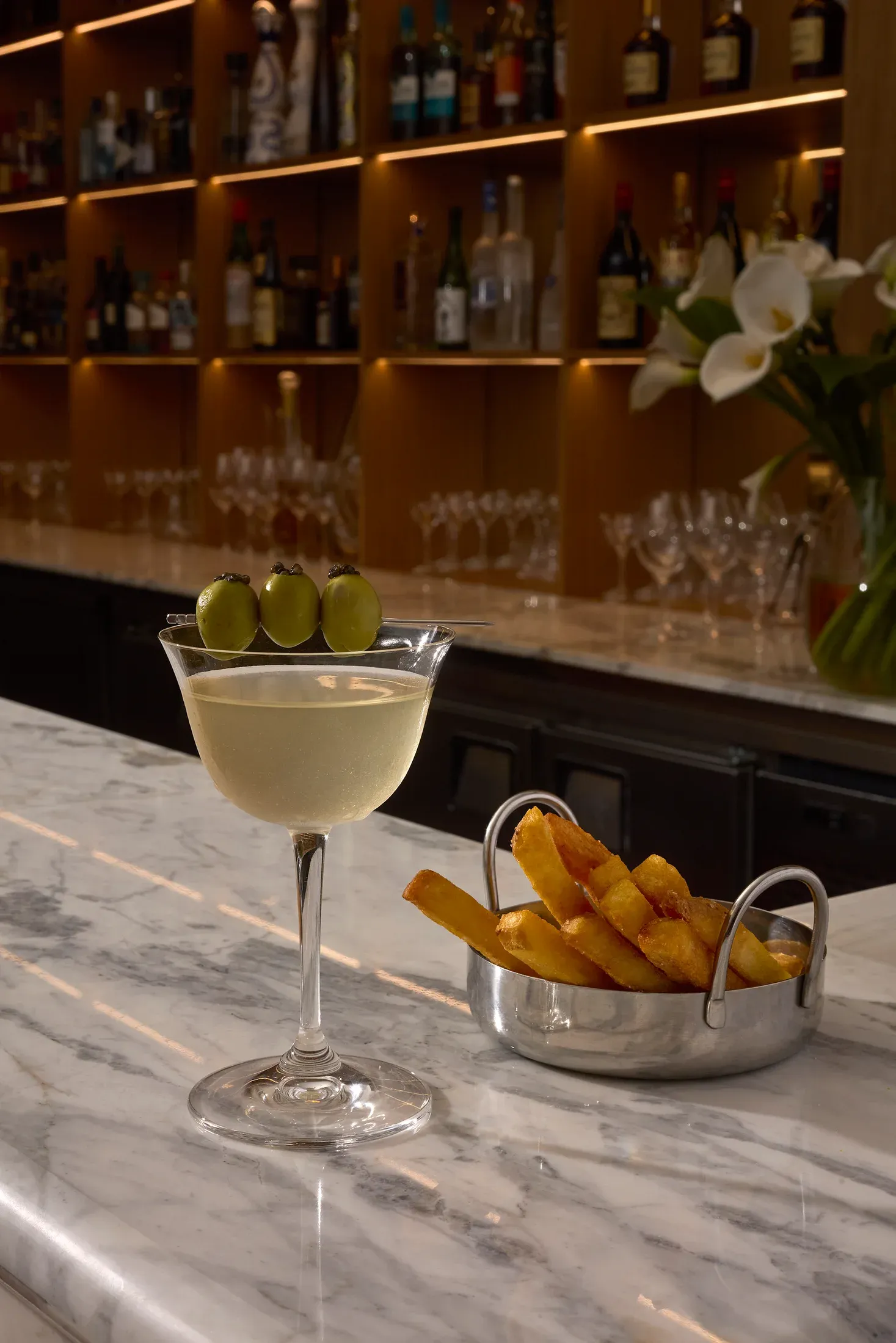 Un cocktail servido en la barra de mármol, con la estantería de botellas detrás