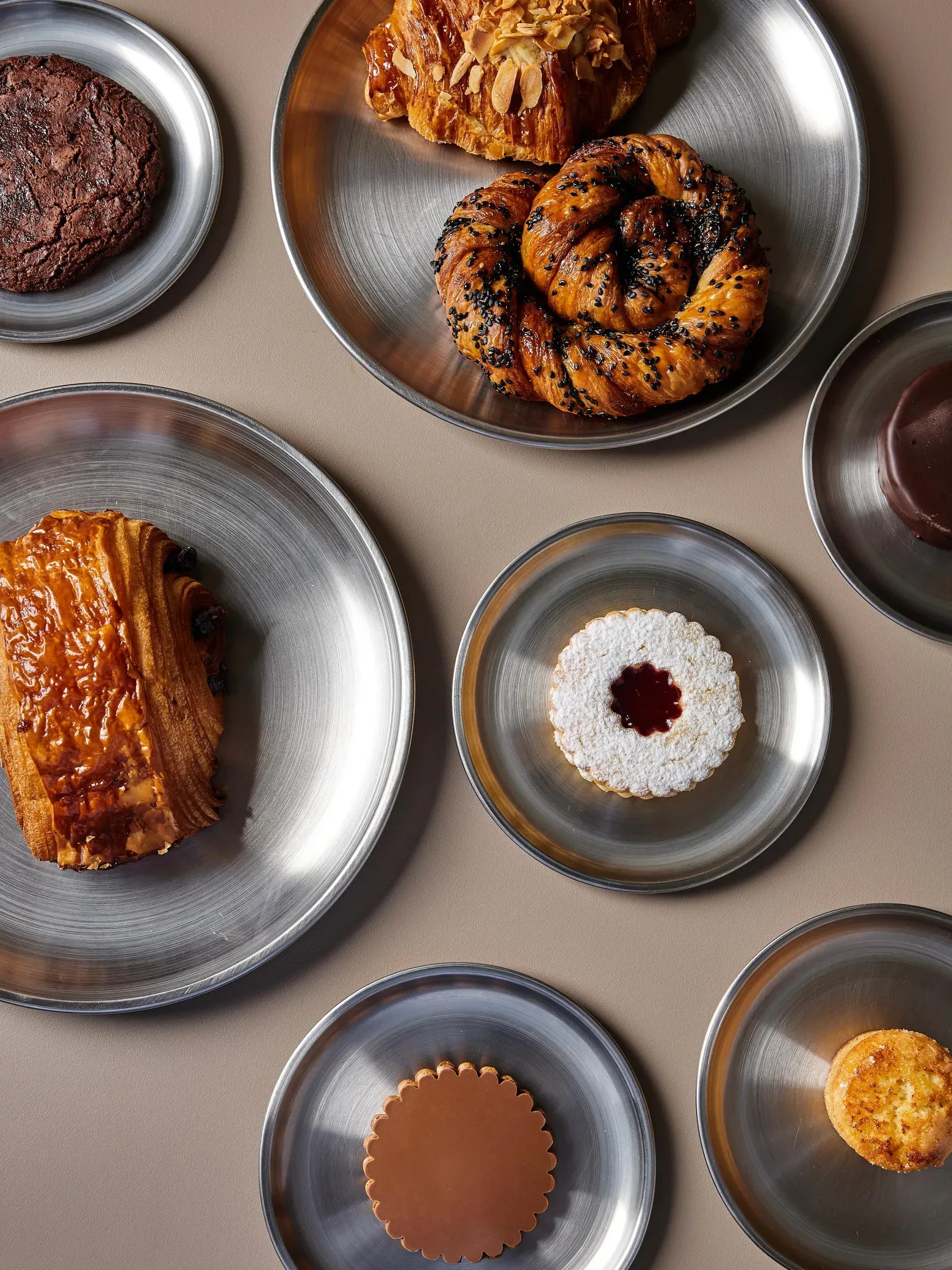Pastelería artesanal del Presencia Gran Café servida en platos de metal: croissant de almendras, pain au chocolat, alfajor y masas finas